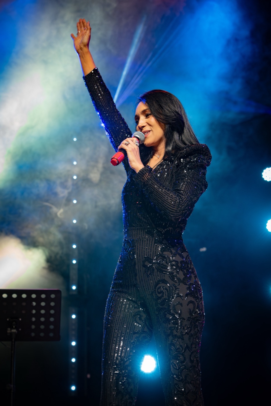 Rebeca Aldana con el brazo en alto entre humo azul de escenario