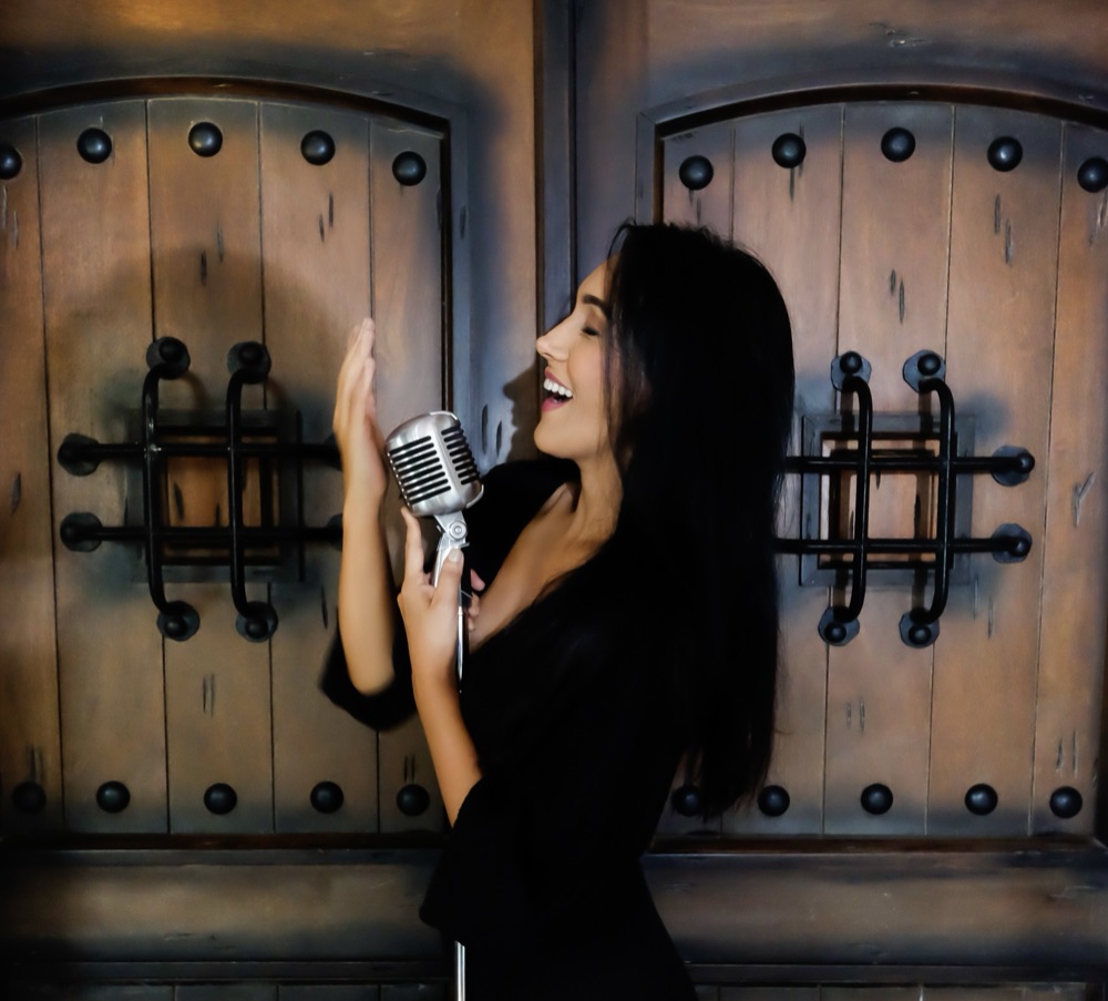 Rebeca Aldana cantando ante una puerta colonial de madera